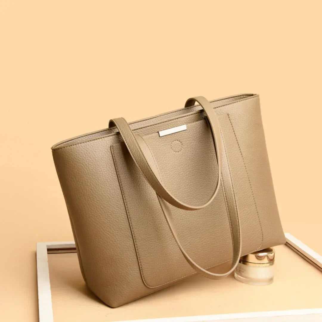 Taupe leather tote bag with double handles on a beige background, stylish womens handbag