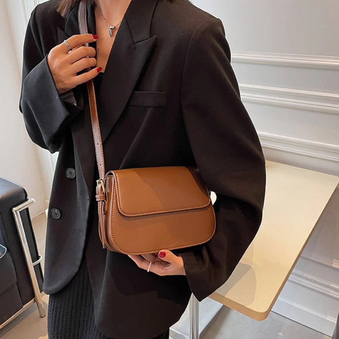 Woman in black blazer holding brown leather crossbody bag indoors