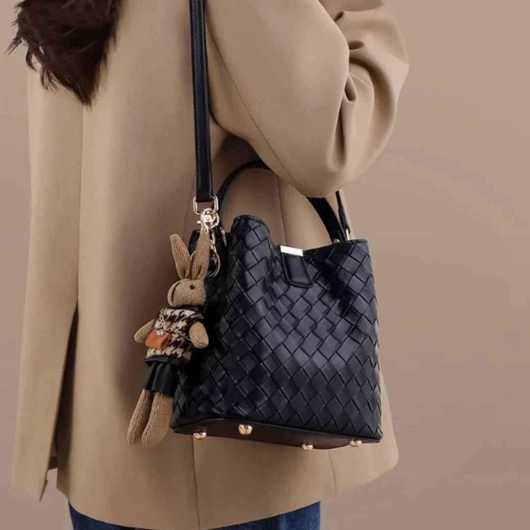 Woman with beige coat holding black woven handbag with bunny keychain accessory
