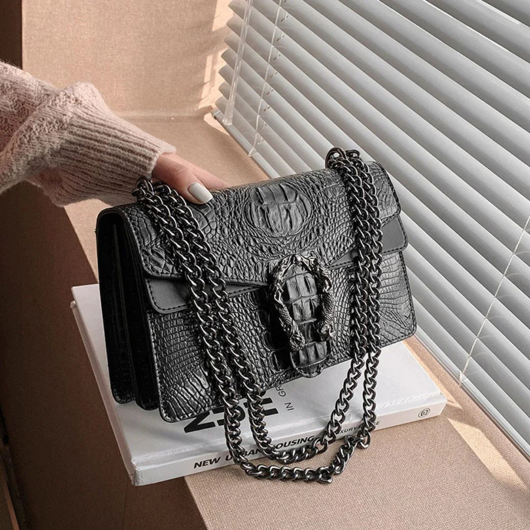 Black crocodile pattern chain shoulder bag on table by window blinds