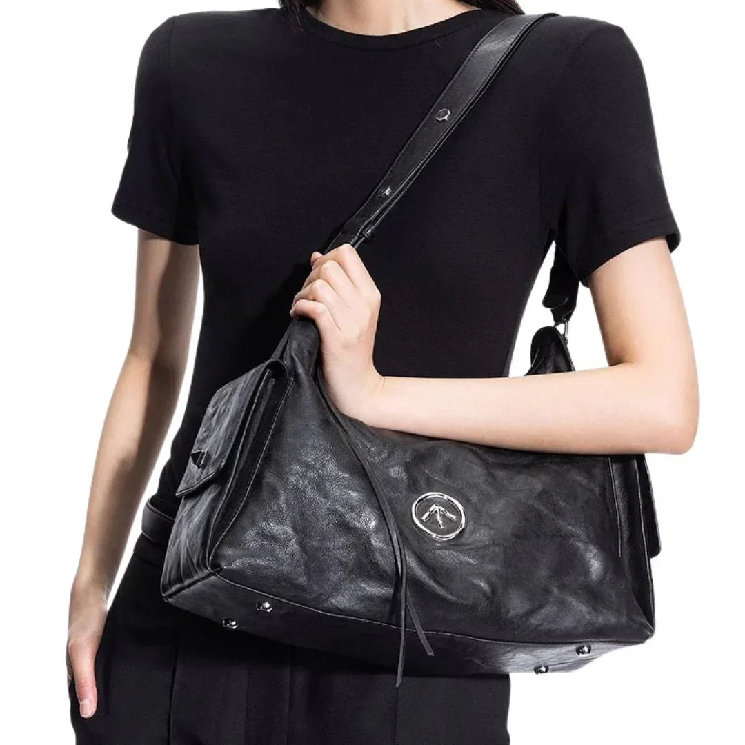 Woman in black shirt carrying a large black leather shoulder bag with logo emblem