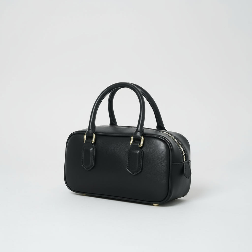 Black leather handbag with gold hardware and double handles on a white background