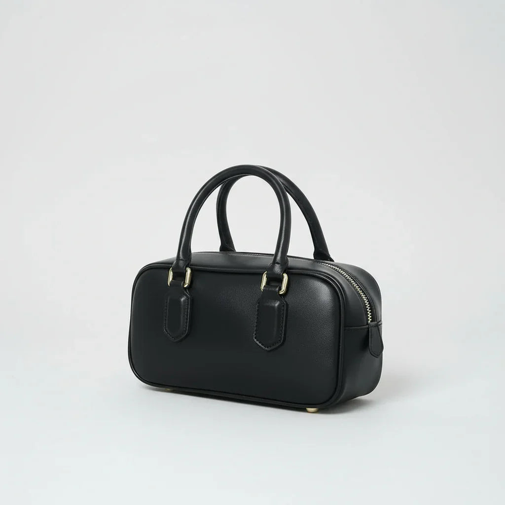 Black leather handbag with gold hardware and double handles on a white background