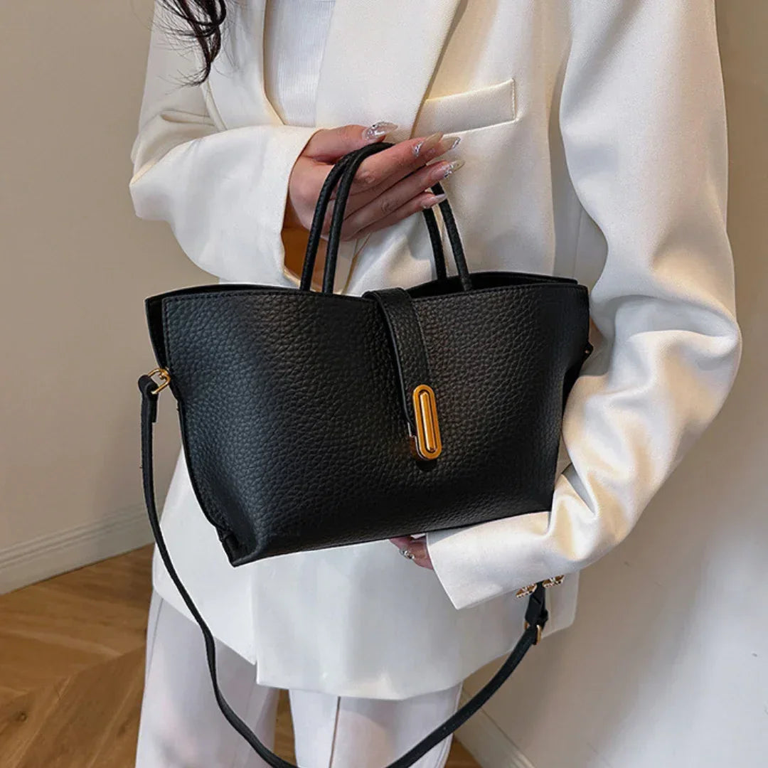 Woman in white suit holding black leather handbag with gold accent and shoulder strap