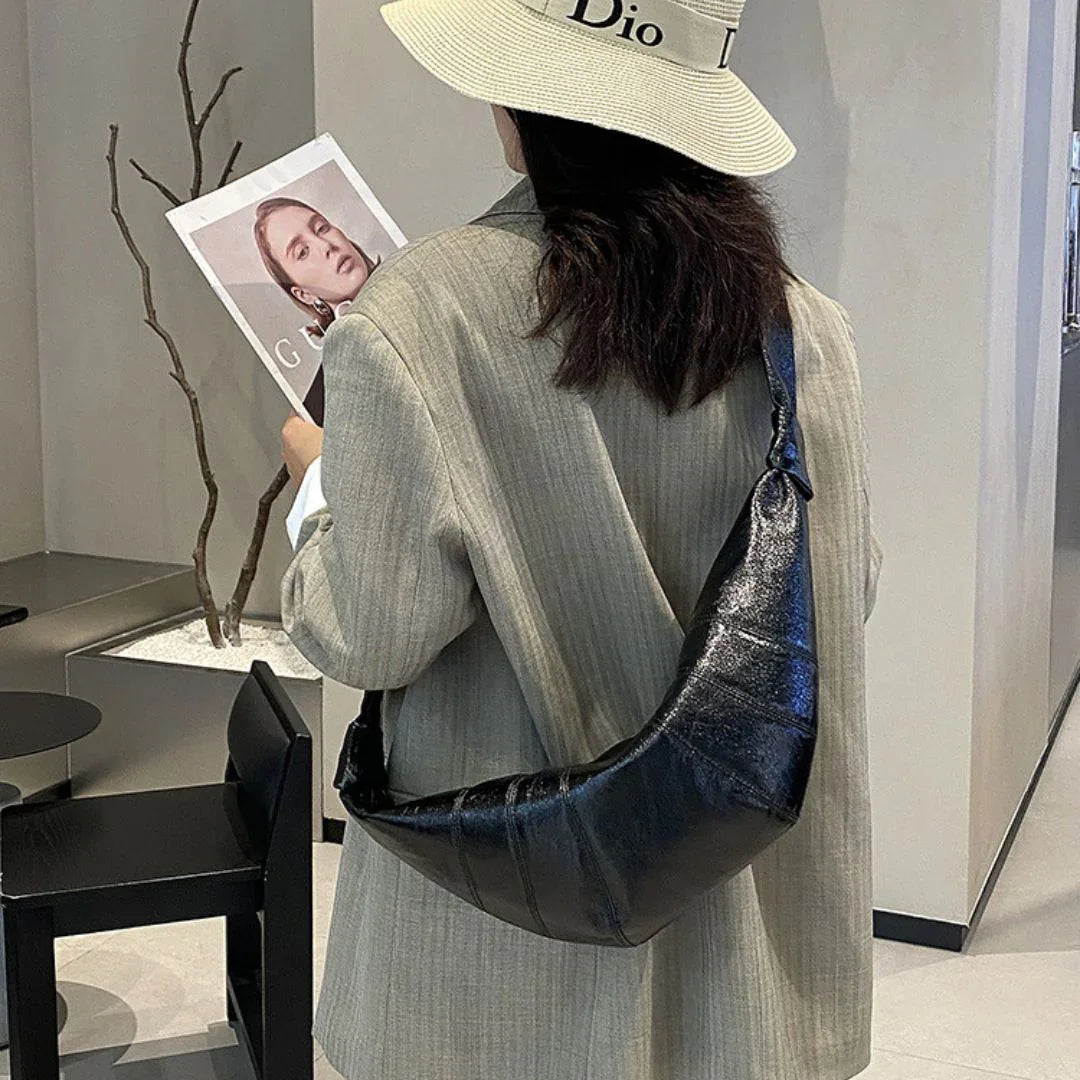 Woman in beige blazer and Dior hat with black crescent shoulder bag, holding magazine indoors