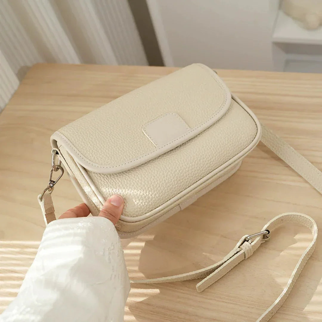 Beige leather crossbody bag with textured finish on light wooden table
