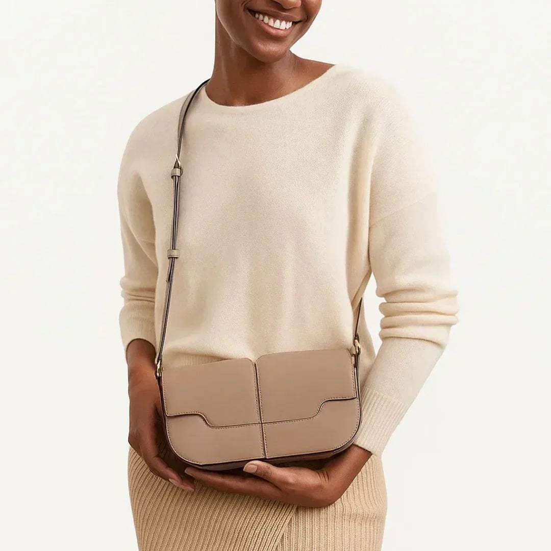 Woman in cream sweater with beige crossbody leather handbag against neutral background