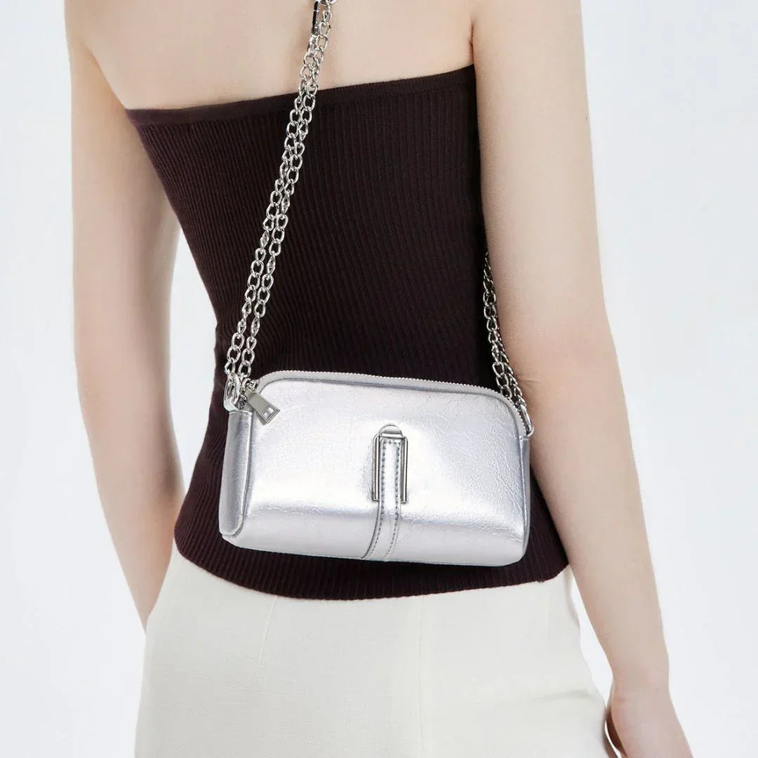 Woman wearing a silver crossbody purse with chain strap, black top and white pants