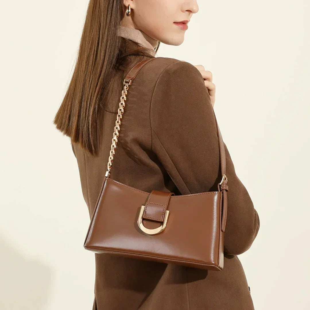Woman in brown coat with a brown leather shoulder bag featuring gold chain strap and buckle.