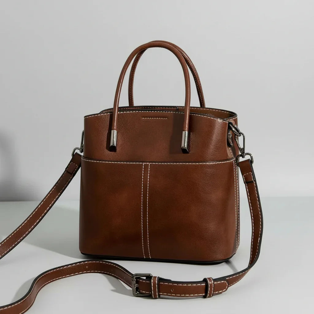 Brown leather handbag with handles and adjustable strap on white background