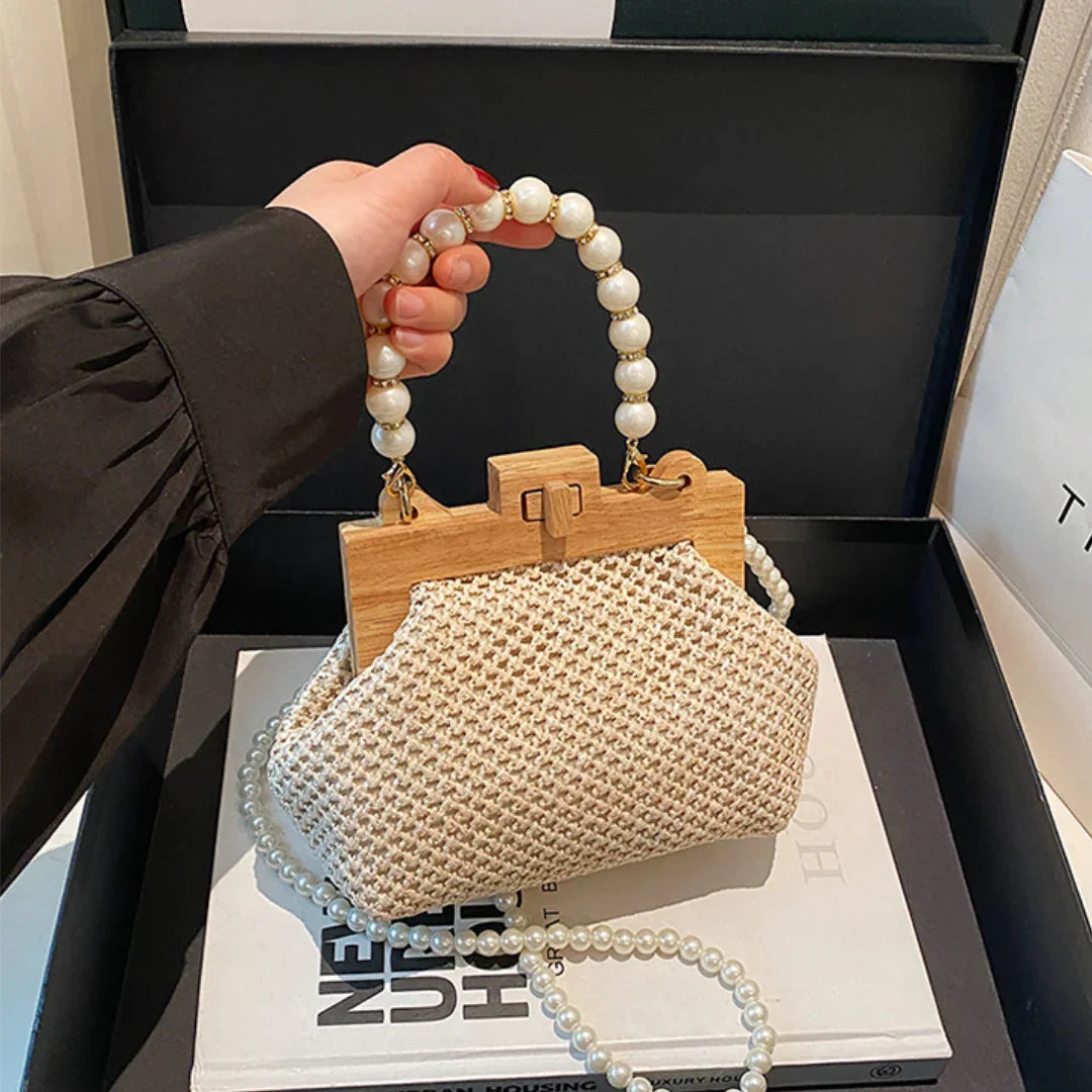Hand holding woven straw handbag with wooden frame and pearl beaded handle in gift box