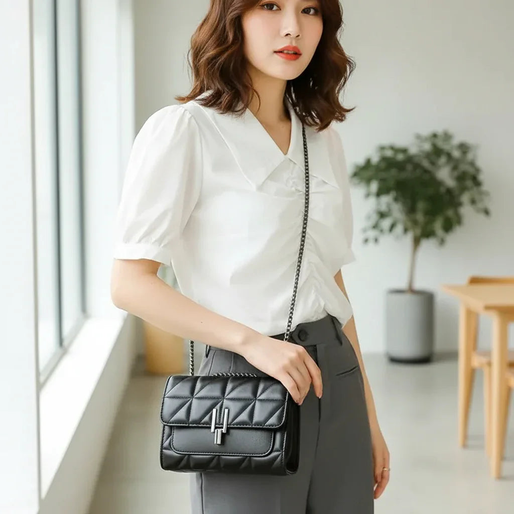 Woman in white blouse and gray pants with black quilted crossbody handbag, indoor setting