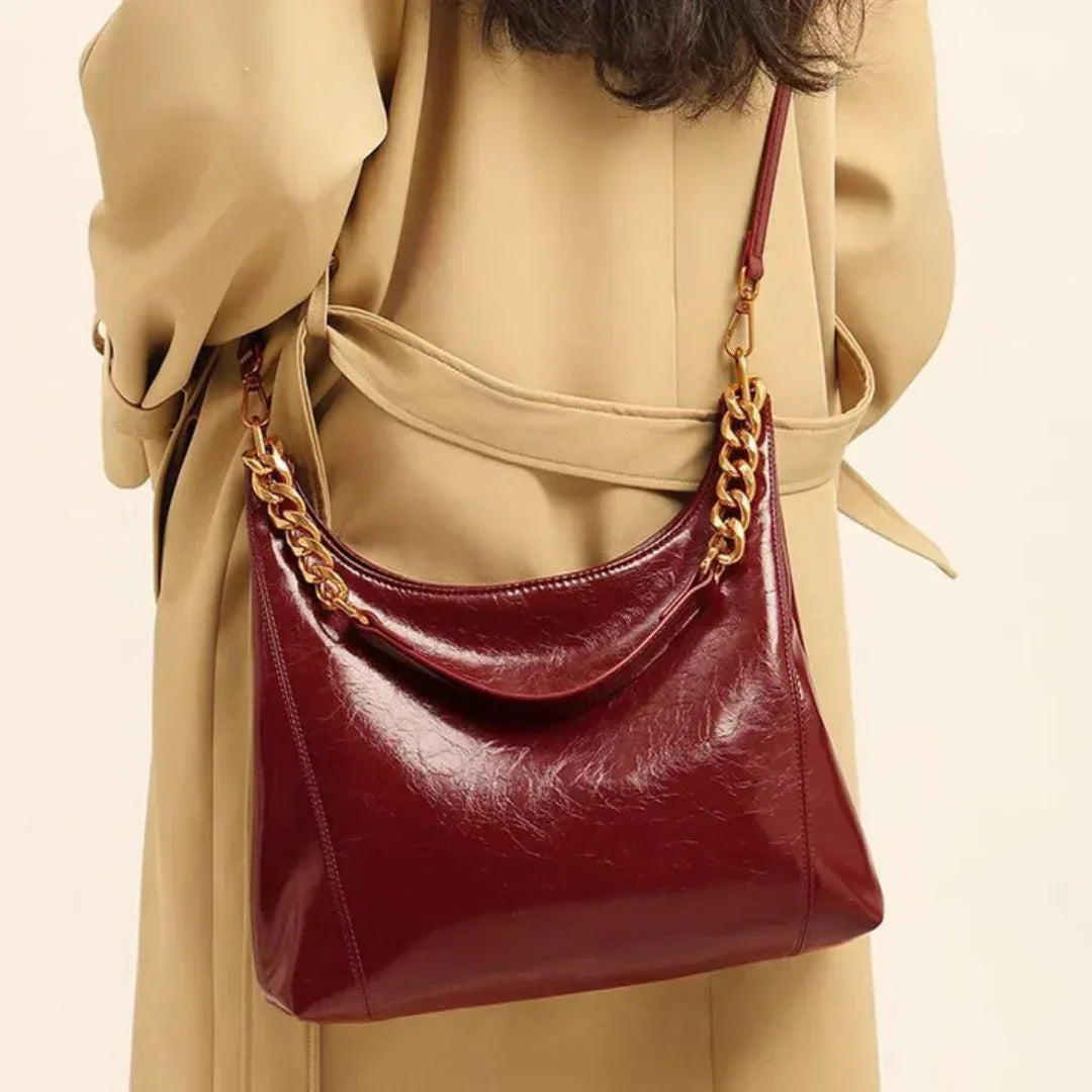 Burgundy leather shoulder bag with gold chain strap on beige trench coat