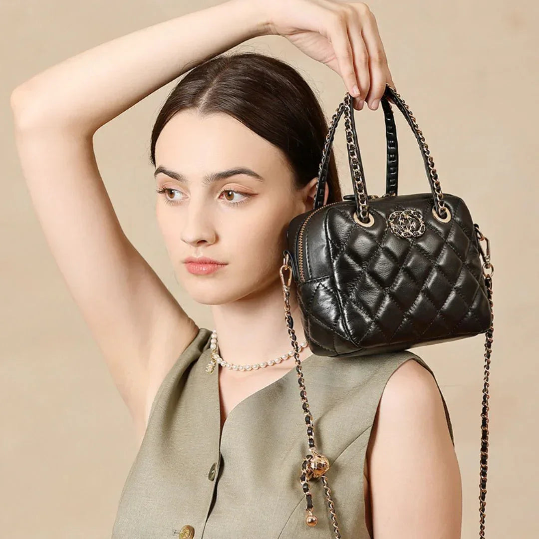 Woman in beige top holding black quilted leather handbag with chain strap