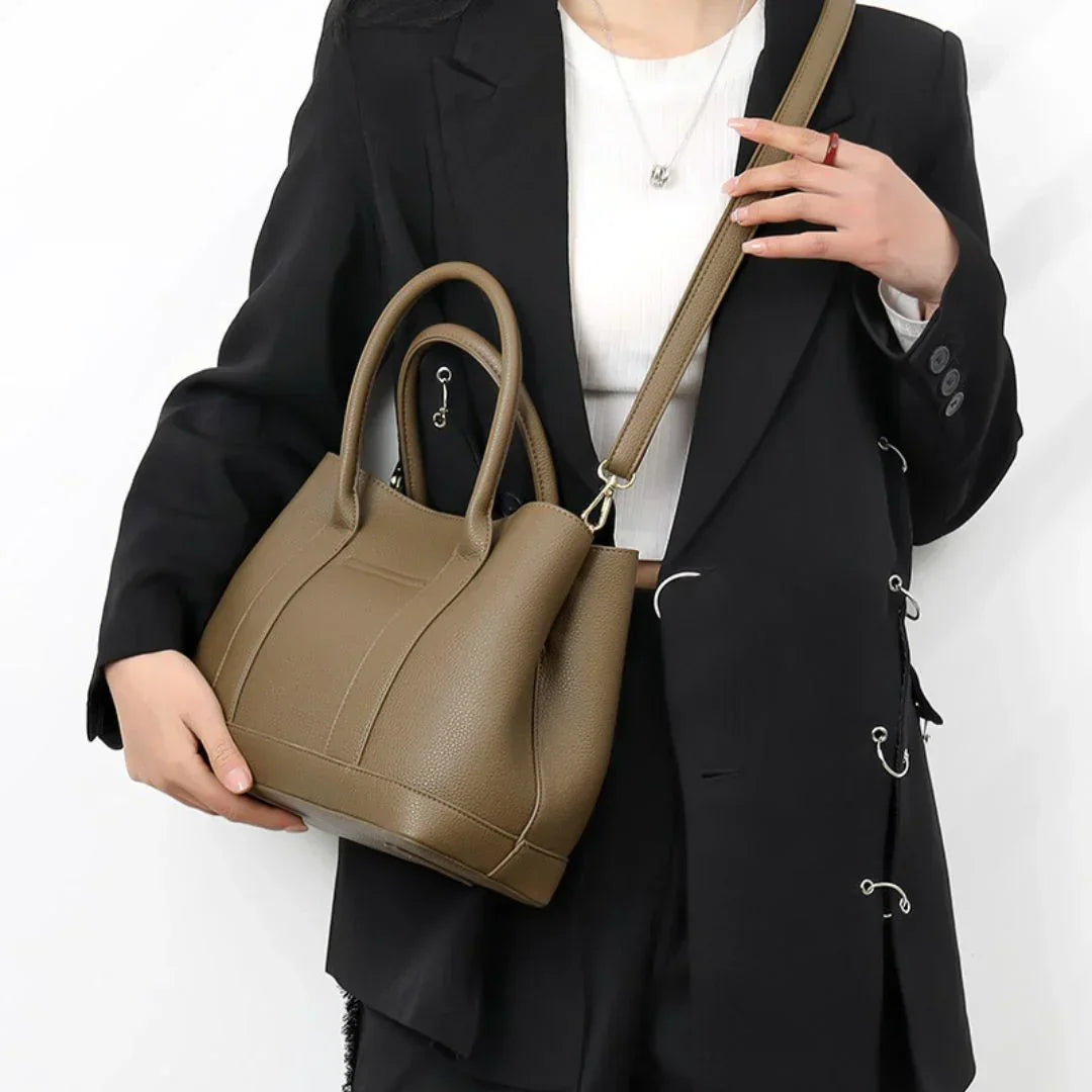 Woman in black blazer holding taupe leather handbag with shoulder strap