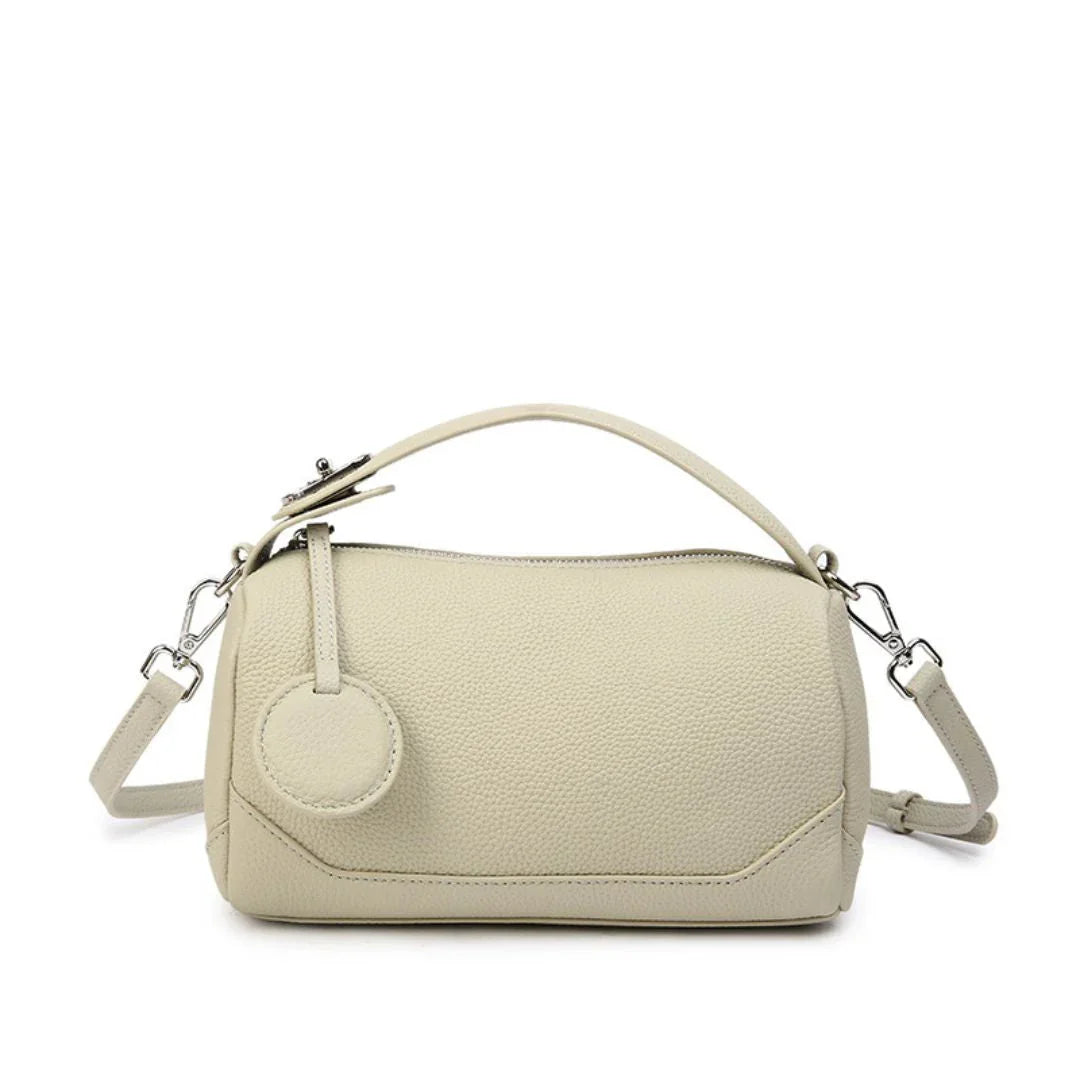 Beige leather shoulder bag with top handle, detachable strap, and circular accent