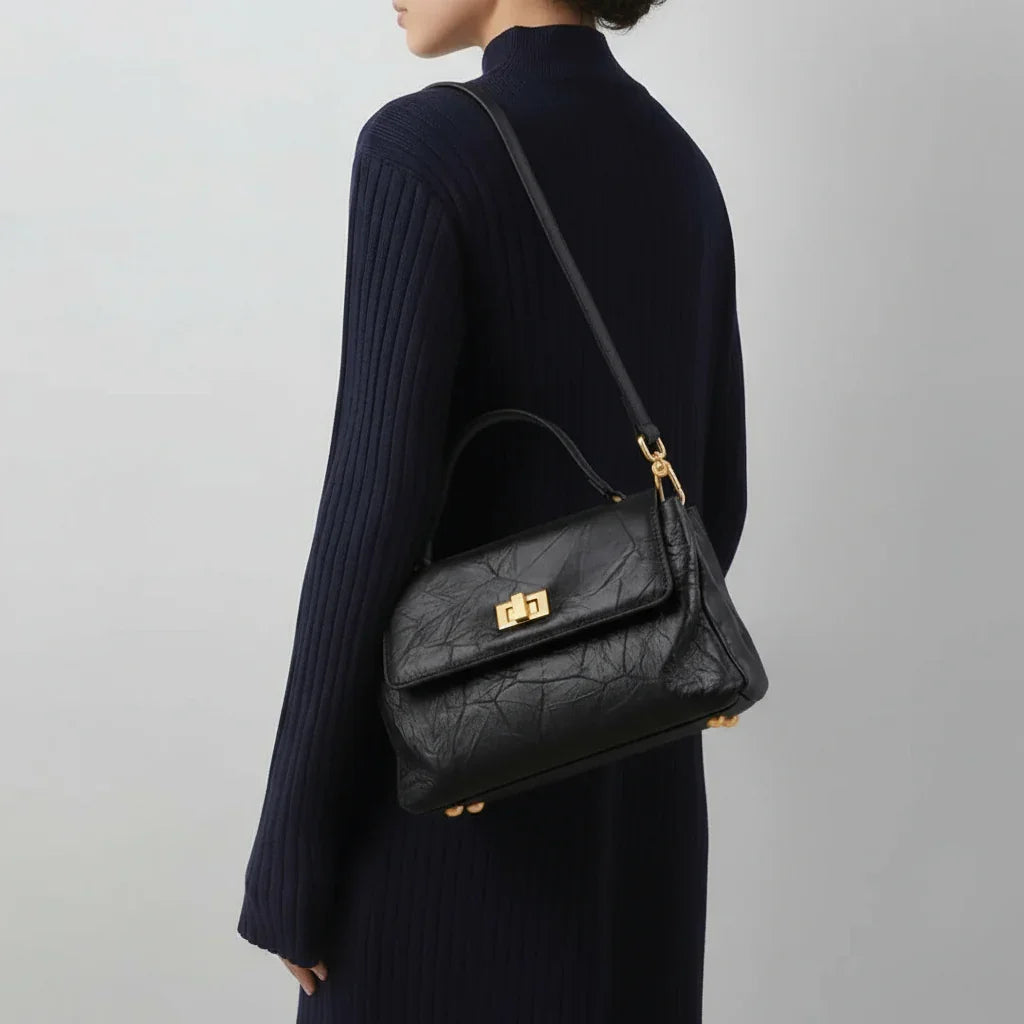Woman in navy ribbed dress carrying black leather shoulder bag with gold hardware