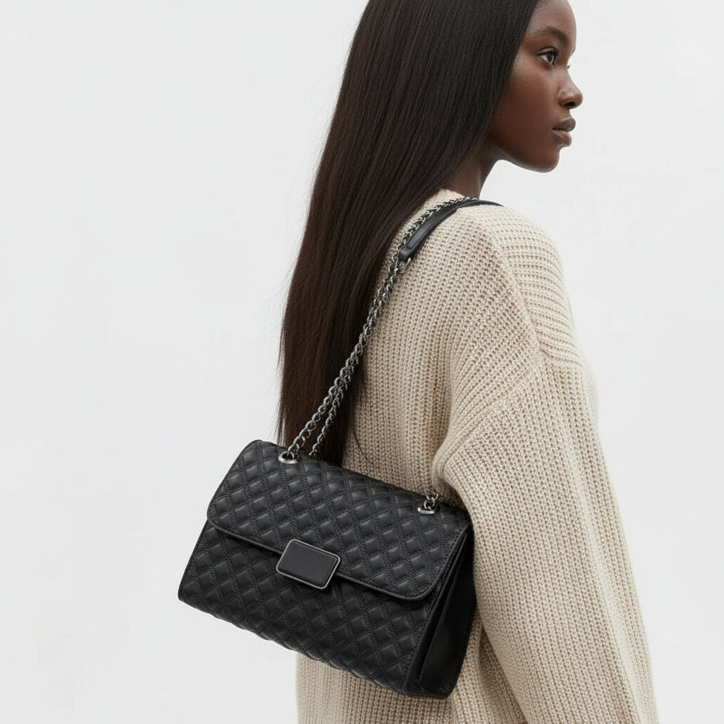 Woman wearing cream sweater with black quilted leather shoulder bag and chain strap
