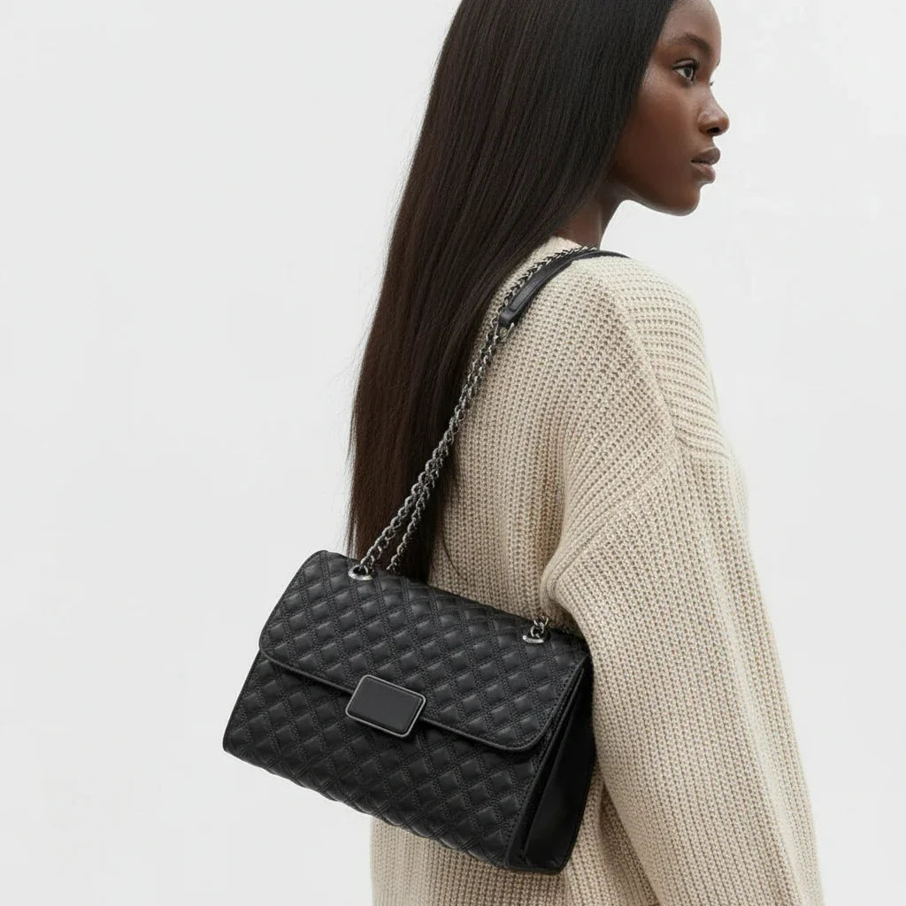 Woman wearing cream sweater with black quilted leather shoulder bag and chain strap