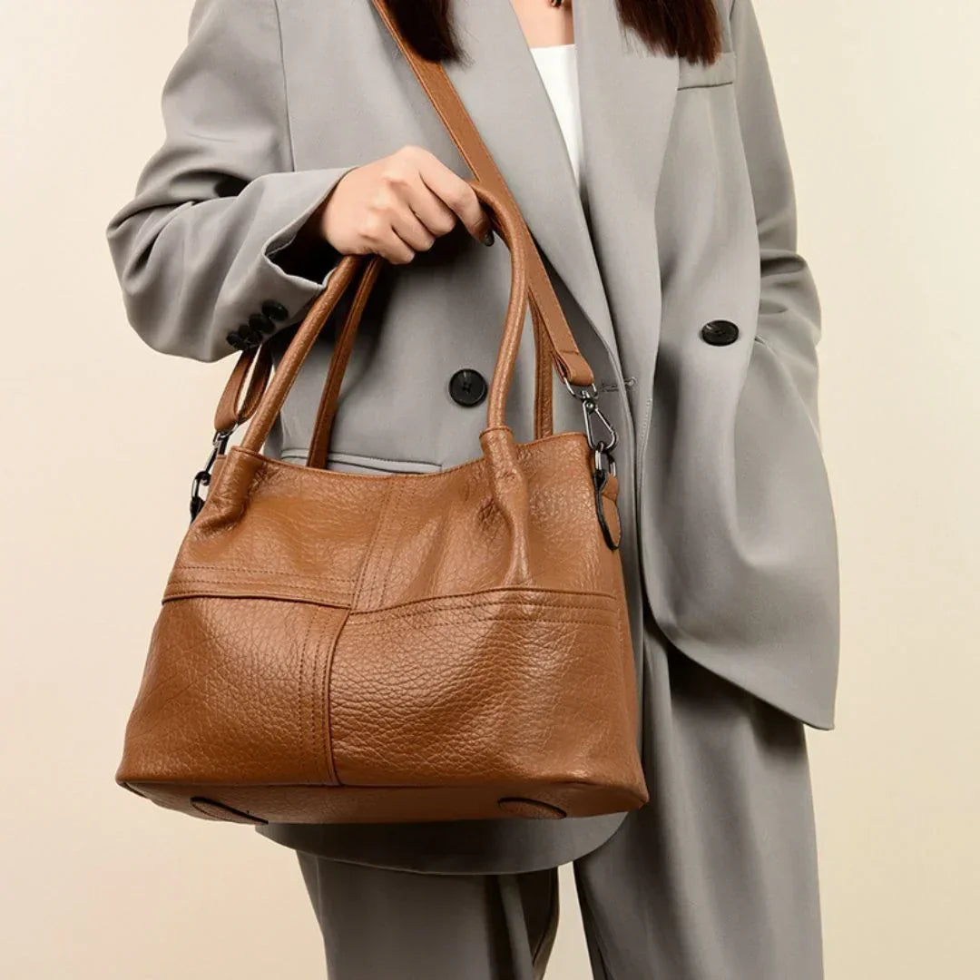 Woman in grey suit holding a large brown leather shoulder bag