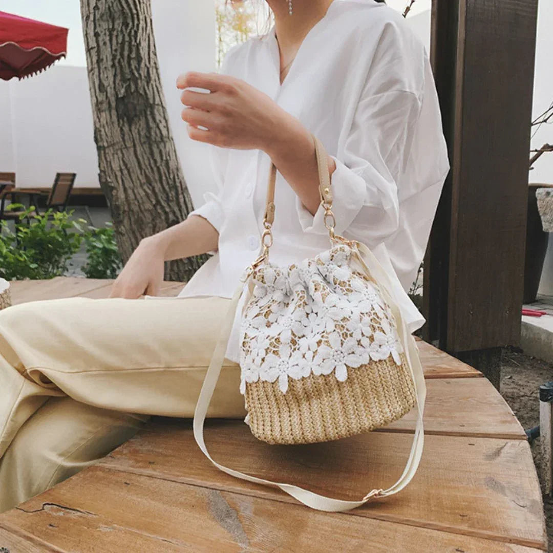 Woman in white blouse and beige pants with lace straw bucket bag at outdoor wooden table