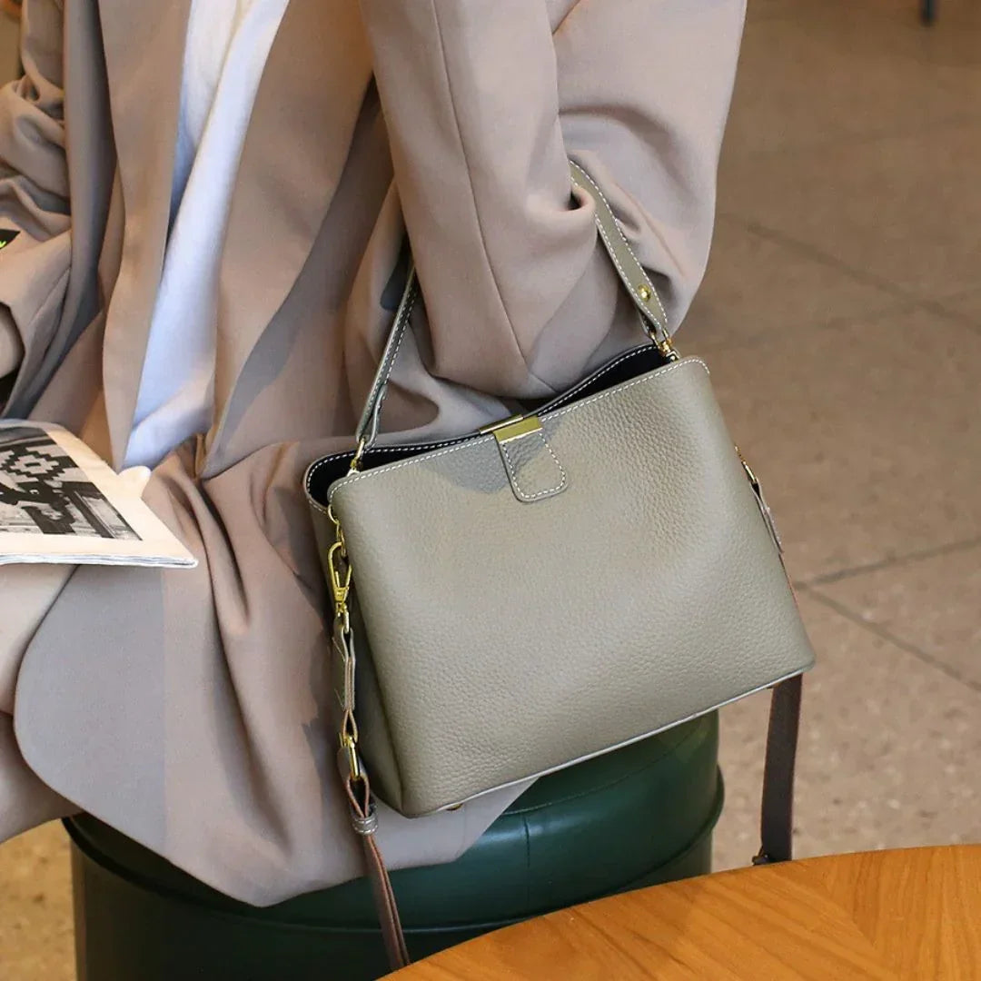 Woman in beige blazer holding newspaper with gray leather handbag in cafe setting