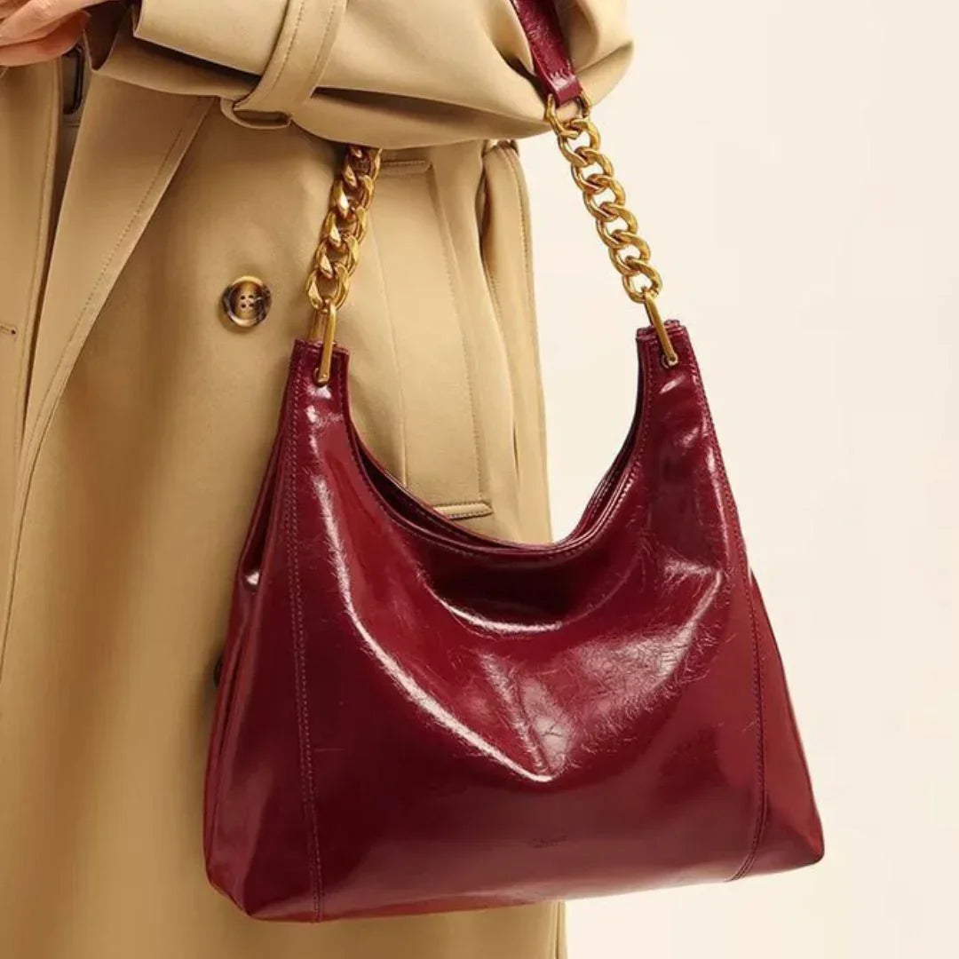 Burgundy leather shoulder bag with gold chain strap on beige trench coat