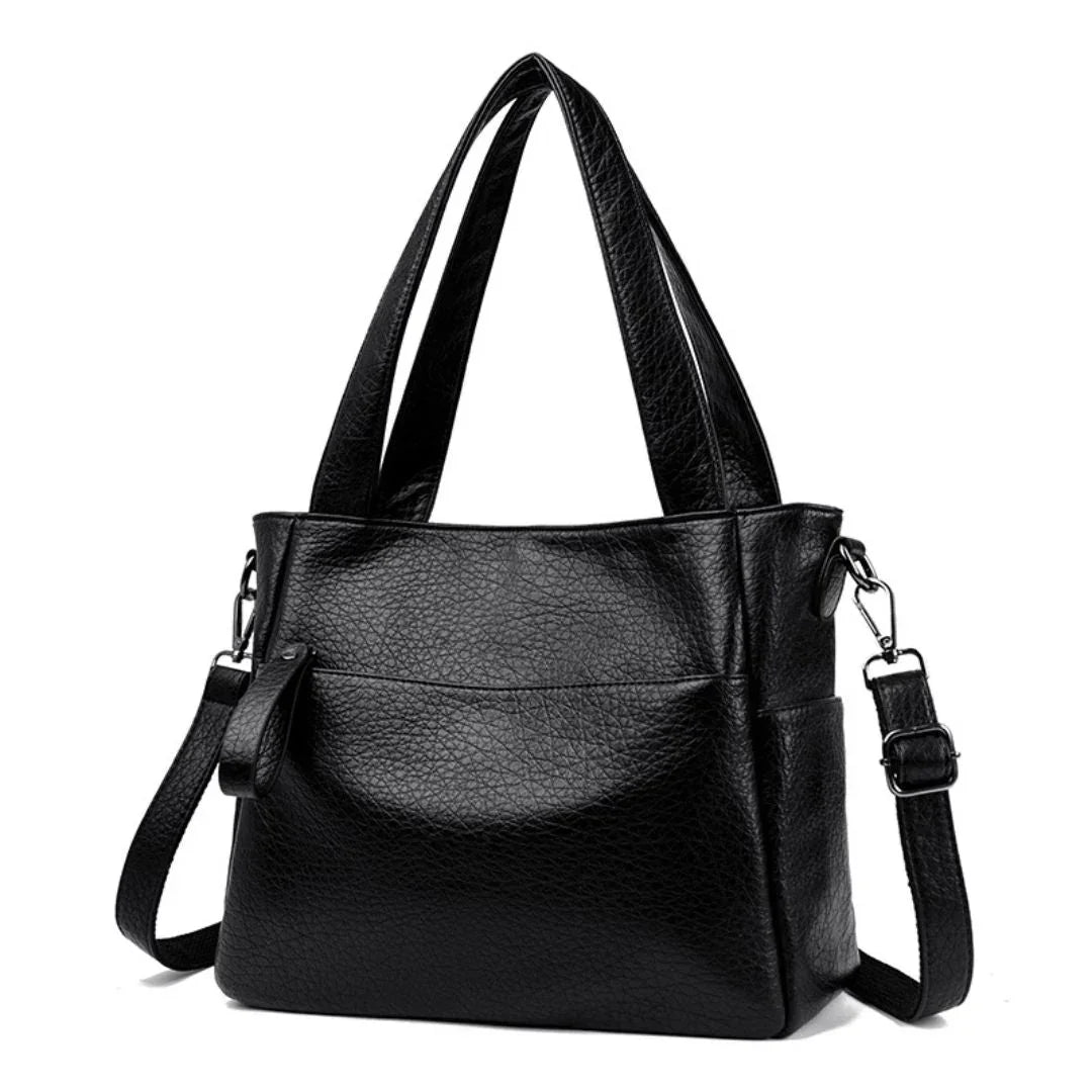 Black leather handbag with double handles and adjustable shoulder strap on white background