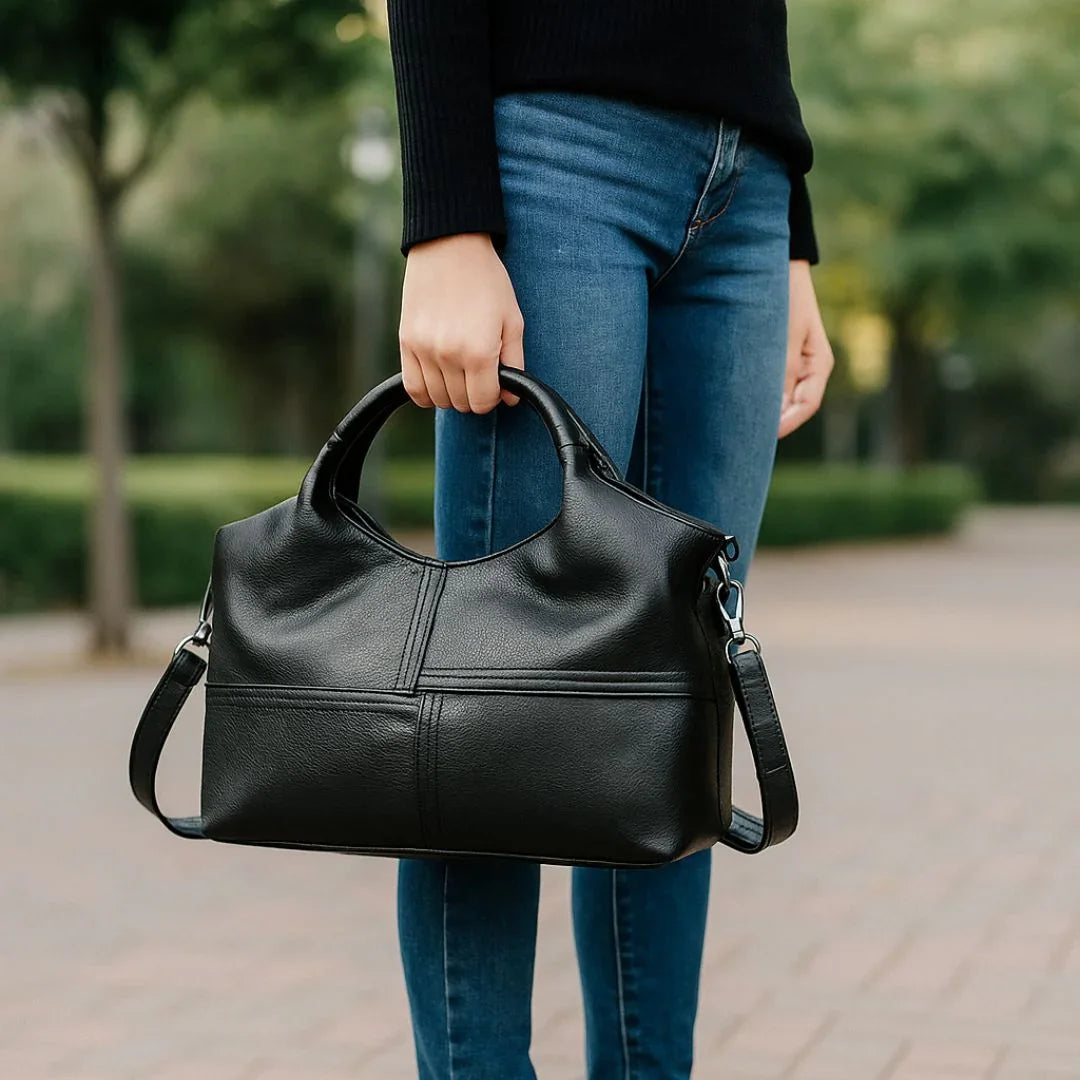 Woman holding black leather handbag outdoors, wearing blue jeans and black sweater