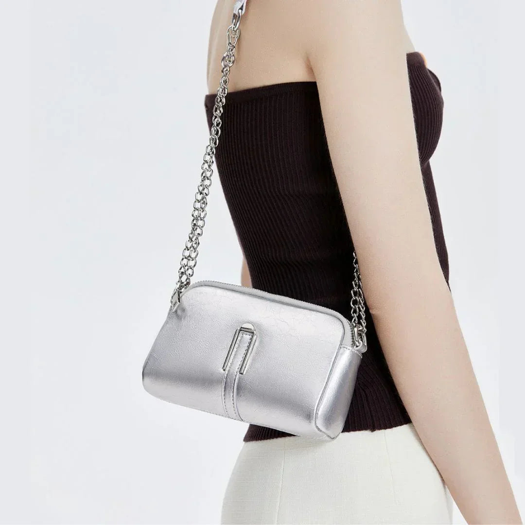 Woman wearing a silver crossbody bag with chain strap, stylish accessory against white background