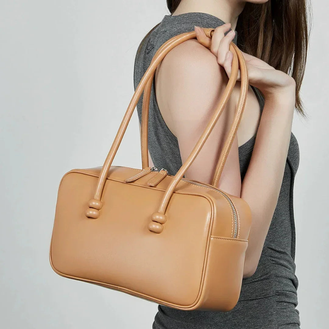 Woman holding tan leather handbag with double handles, neutral background