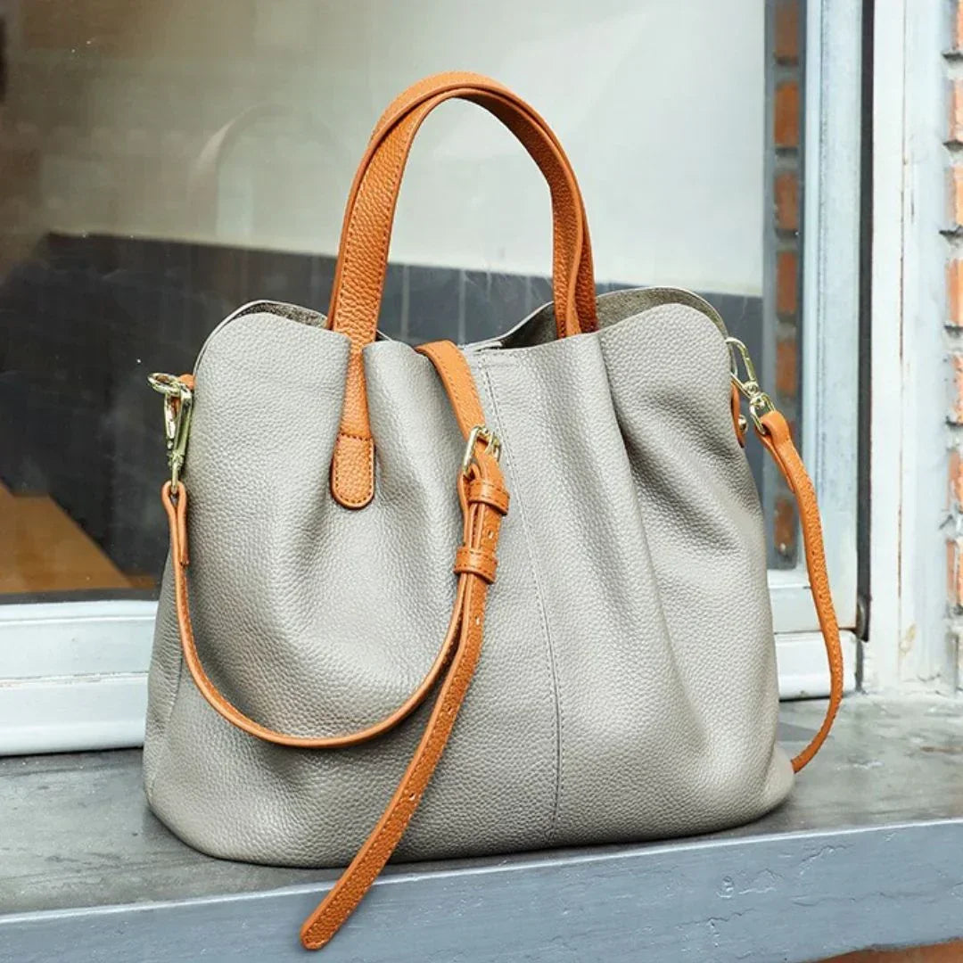 Taupe leather handbag with tan straps on windowsill, stylish women's purse