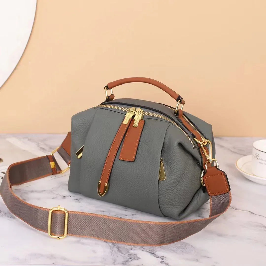Gray leather handbag with brown handles and gold zippers on marble table