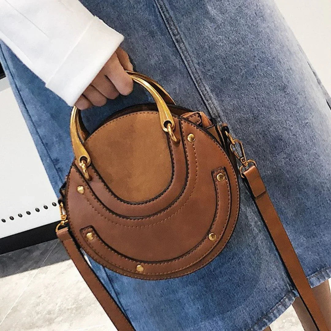 Round brown leather handbag with gold handles, worn over blue denim skirt