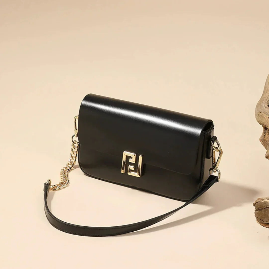 Black leather shoulder bag with gold chain strap and clasp on beige background