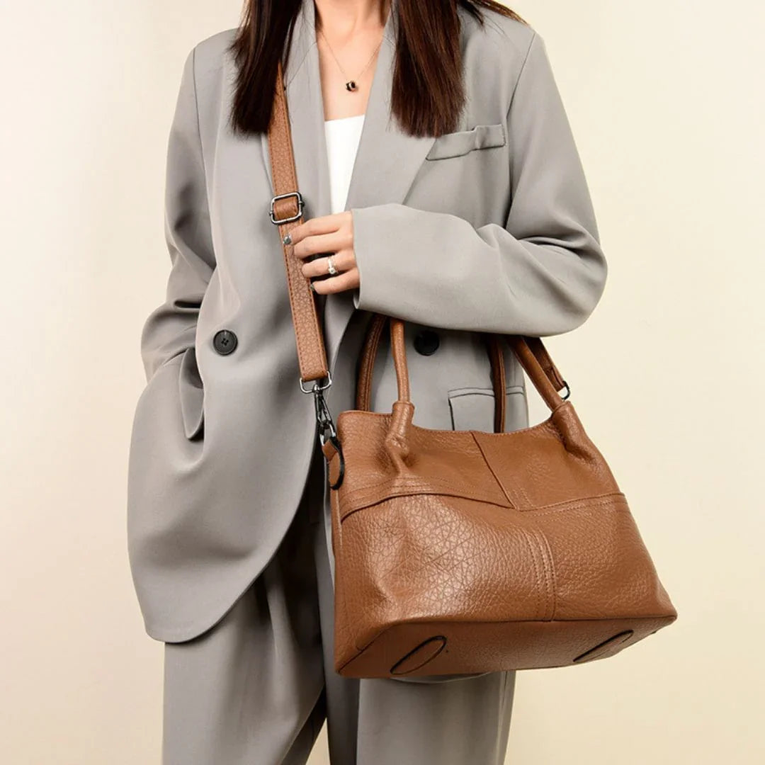 Woman in grey suit carrying a brown leather shoulder bag with top handles