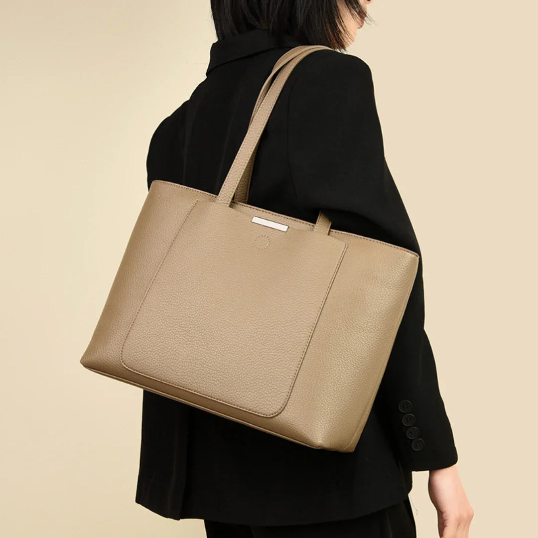 Woman in black blazer carrying taupe leather tote bag on shoulder