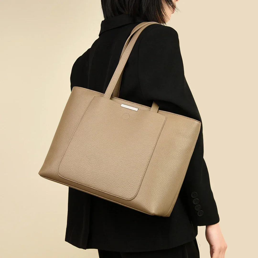 Woman in black blazer carrying taupe leather tote bag on shoulder