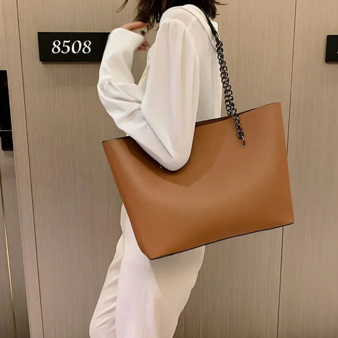 Woman in white outfit holding large brown leather tote bag with chain strap by hotel door 8508