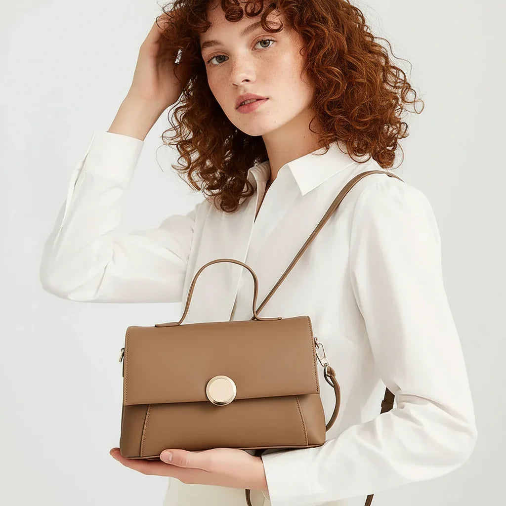 Woman in white blouse holding tan leather crossbody handbag with gold clasp