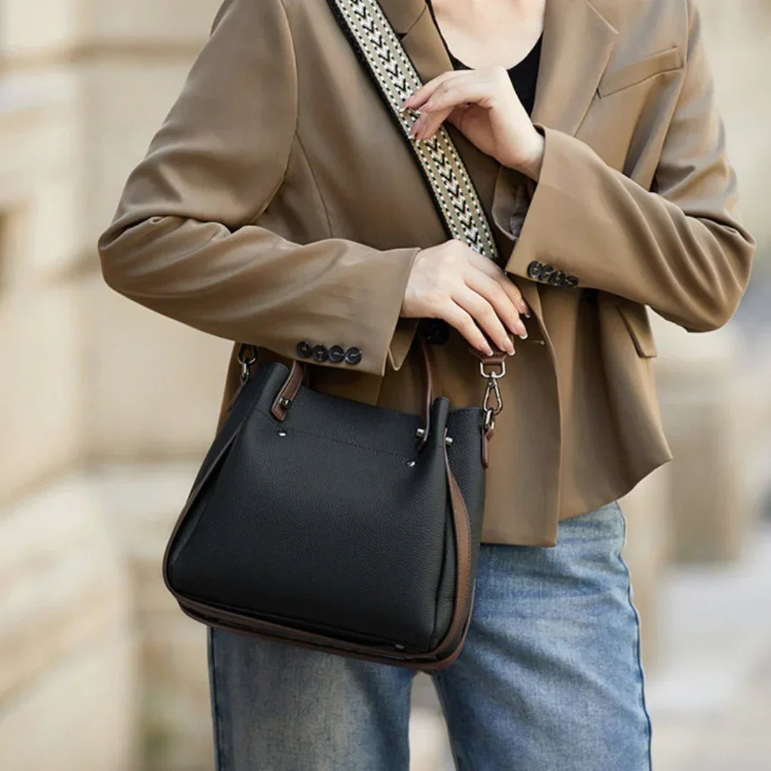 Woman in tan blazer and jeans carrying black leather handbag with patterned strap
