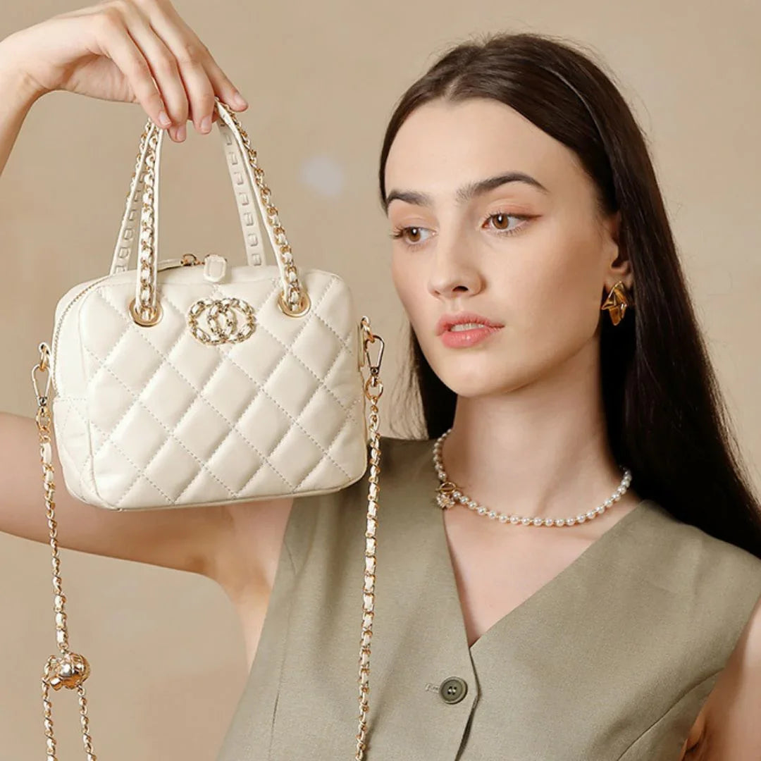 Woman holding quilted ivory handbag with gold chain, wearing sleeveless top and pearl necklace