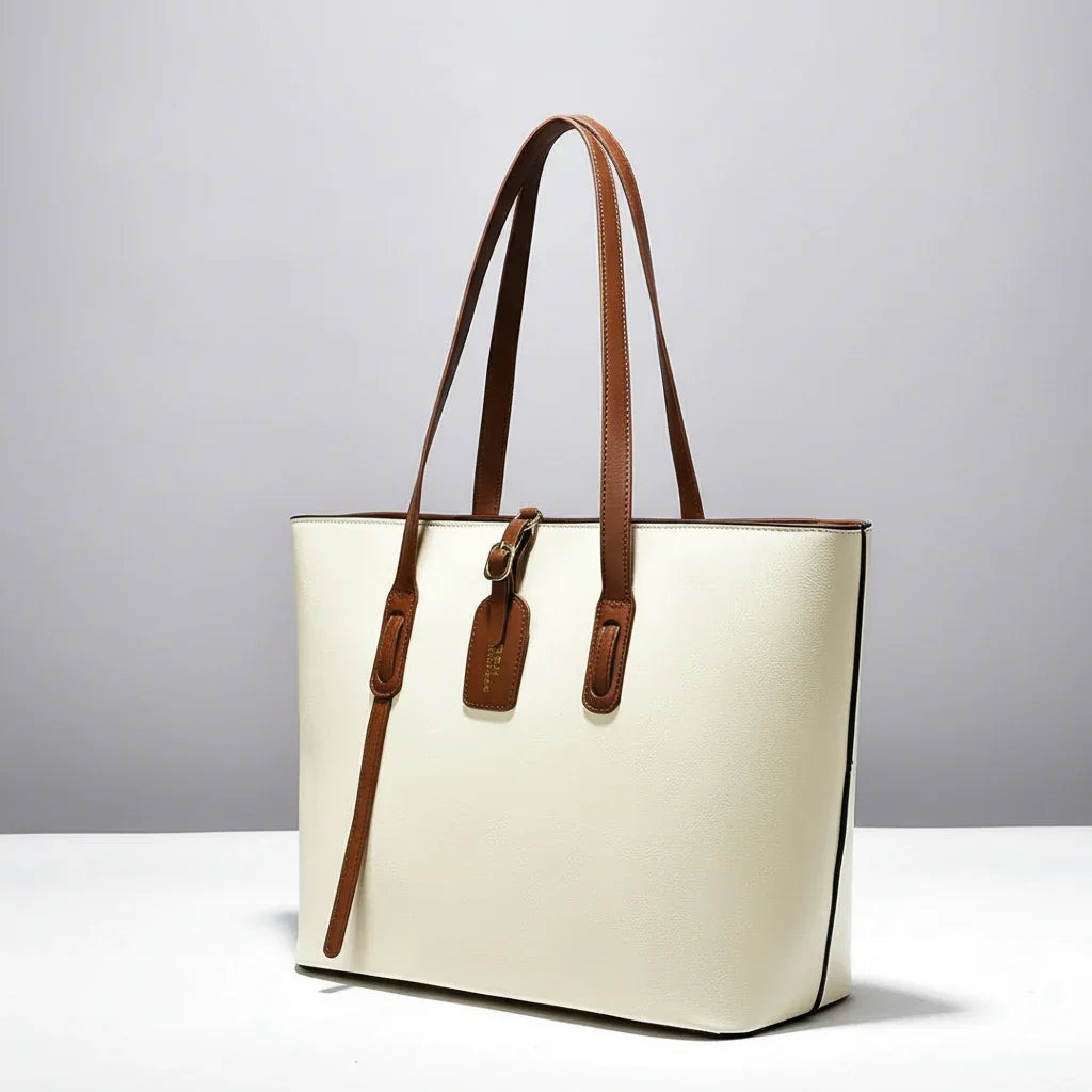 Cream tote bag with brown leather straps on white surface, minimalist handbag