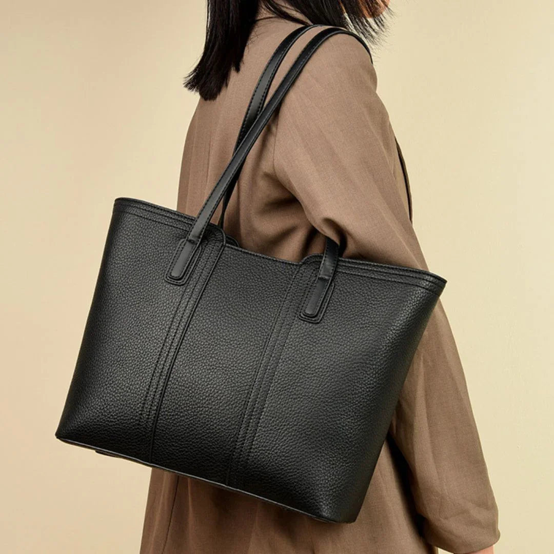 Woman wearing brown coat carrying large black leather tote bag on shoulder