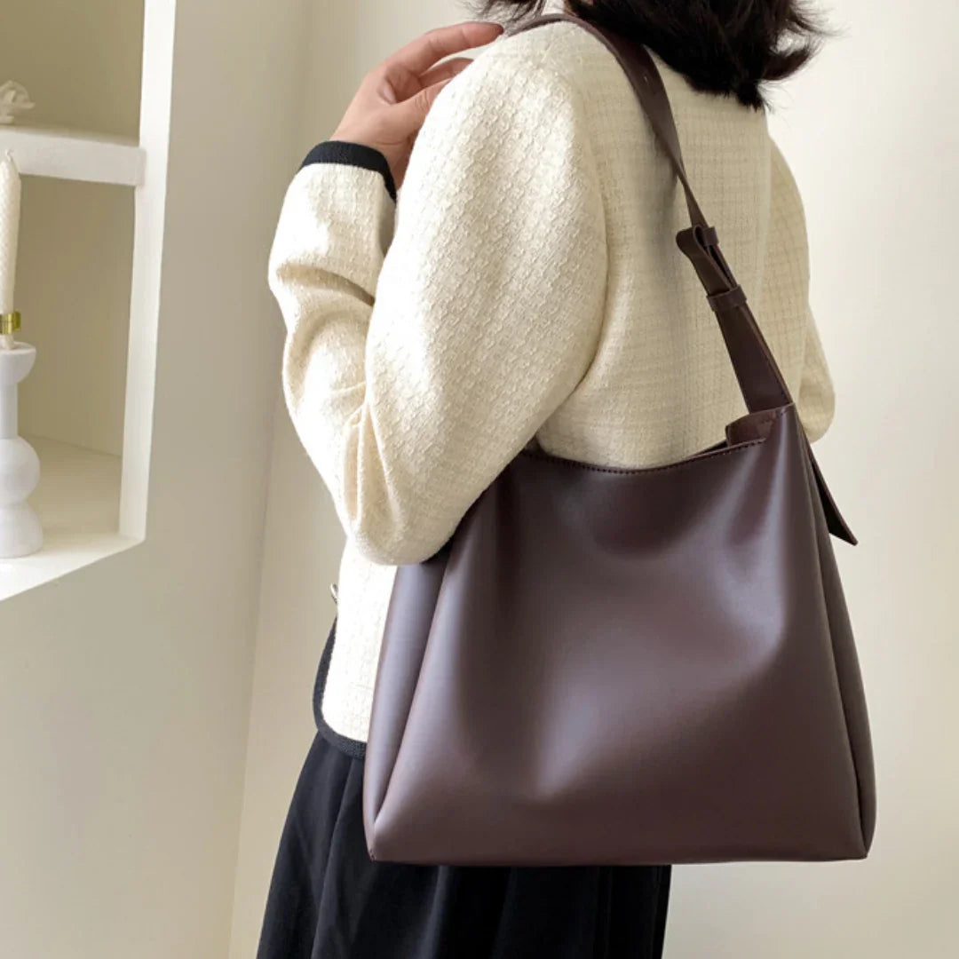 Woman wearing cream textured jacket carrying a brown leather shoulder bag indoors