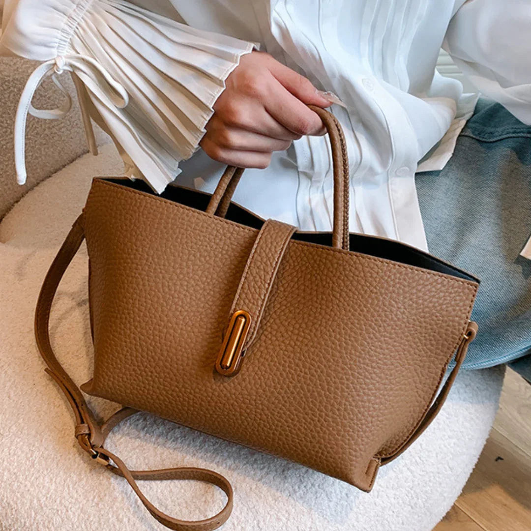 Woman holding a brown leather tote handbag with gold buckle detail and shoulder strap