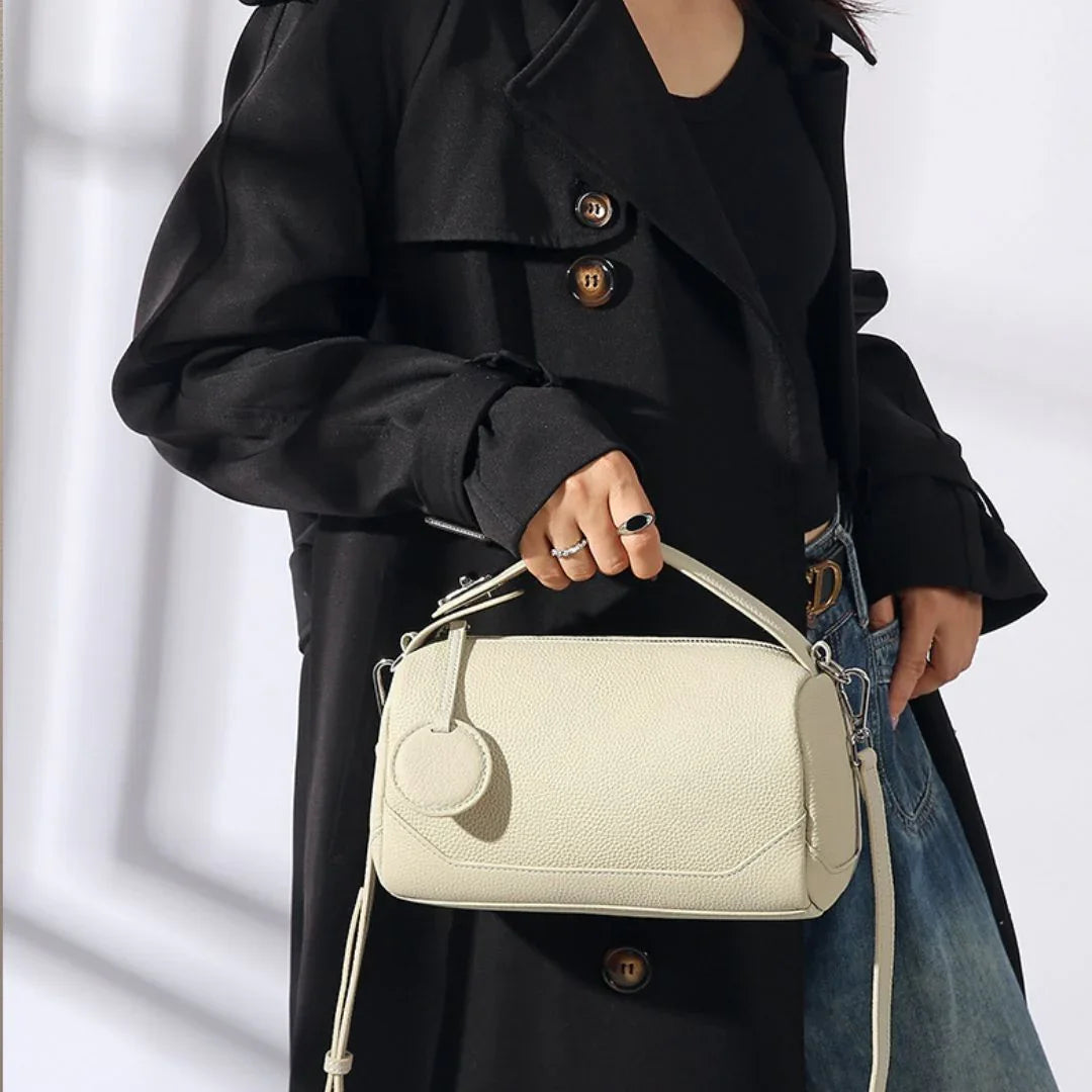 Woman in black trench coat holding a textured cream leather handbag