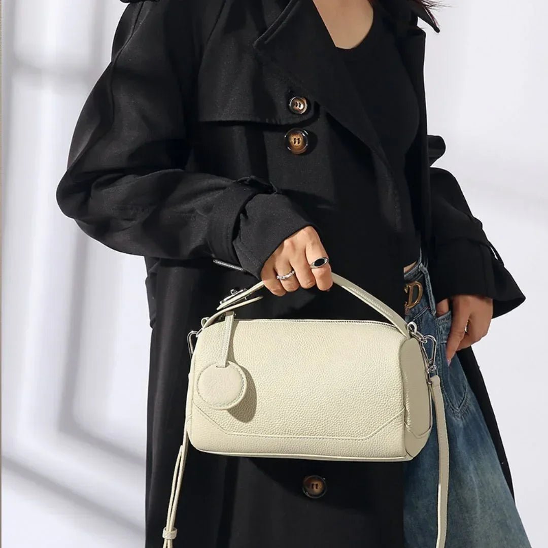 Woman in black trench coat holding a textured cream leather handbag