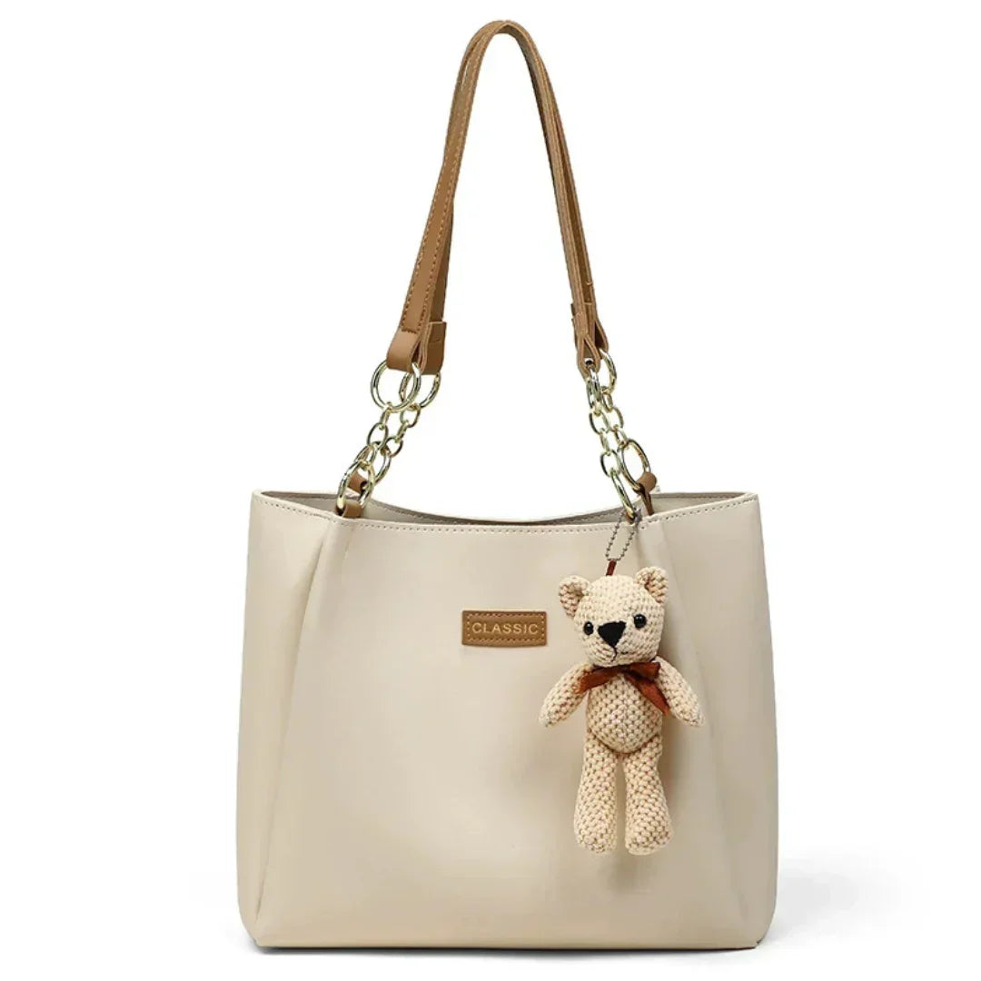 Beige leather tote bag with brown handles, gold chain, and teddy bear keychain charm