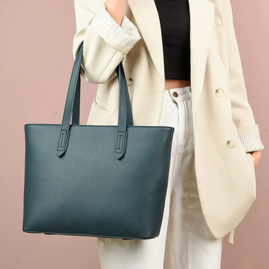 Woman in cream blazer holding large teal leather tote bag against pink background